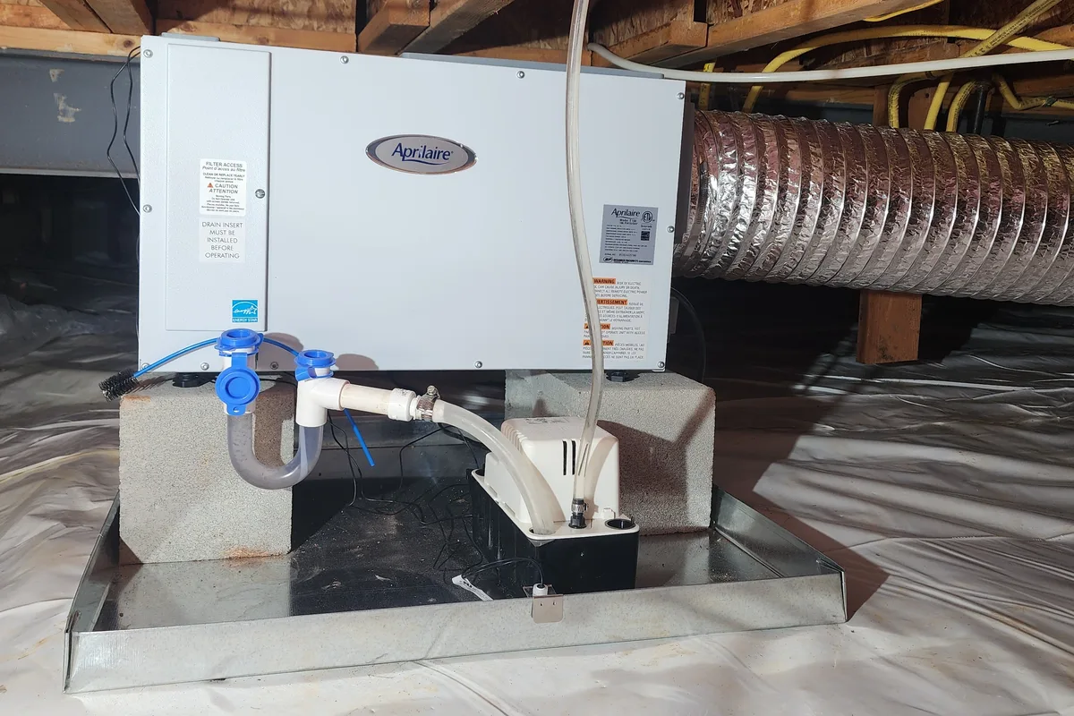 AprilAire dehumidifier installed on concrete blocks in an encapsulated crawl space in Raleigh NC, with condensate pump and insulated ductwork visible