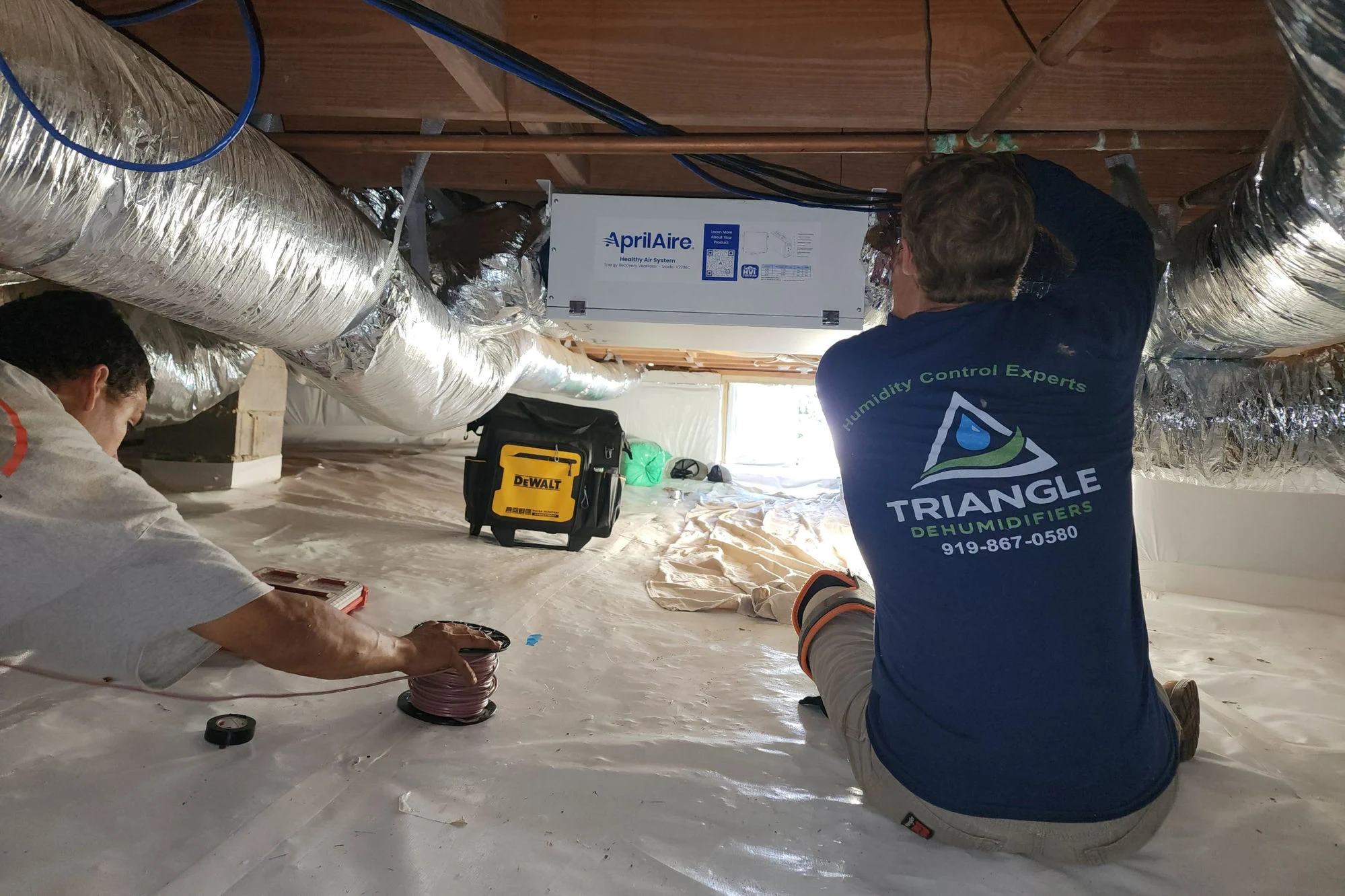 Triangle Dehumidifiers technicians installing an AprilAire Healthy Air System ERV in a Raleigh NC home crawl space — job prompted by CO2 readings consistently above 1,000 ppm in a tightly built home