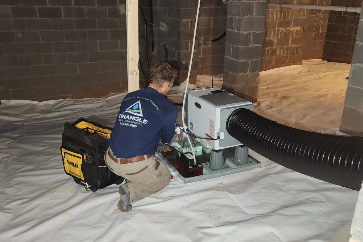 Triangle Dehumidifiers technician installing an AprilAire dehumidifier and duct connection in an encapsulated crawl space in the Triangle NC