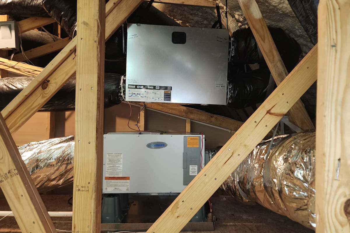 A Broan ERV installed above an AprilAire whole-house dehumidifier in a Wake County NC attic, with fresh-air and exhaust ducts labeled, the two systems working together