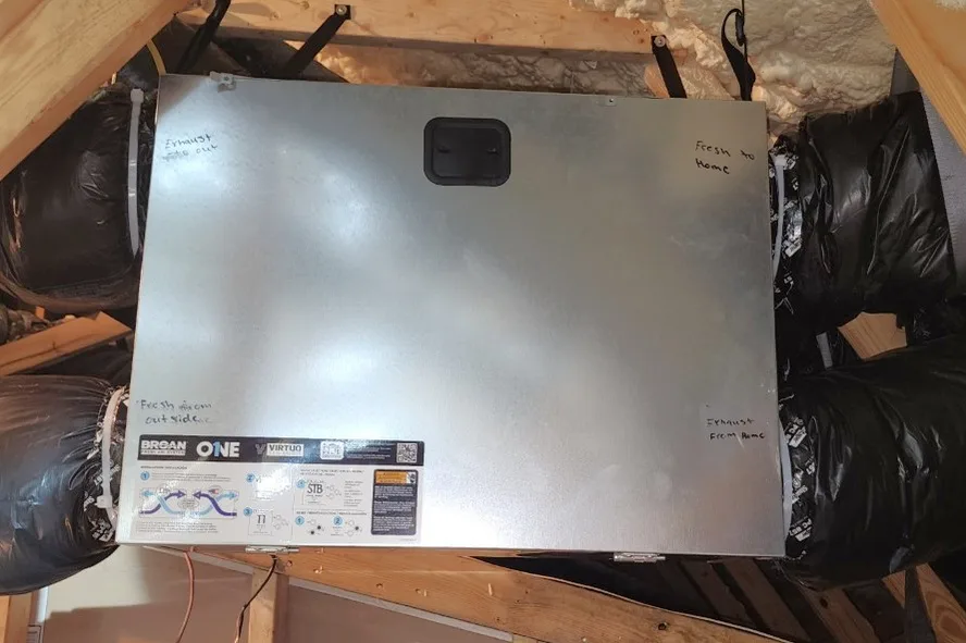Broan ERV hung from the rafters in a Raleigh NC attic with insulated fresh air and exhaust ducts connected