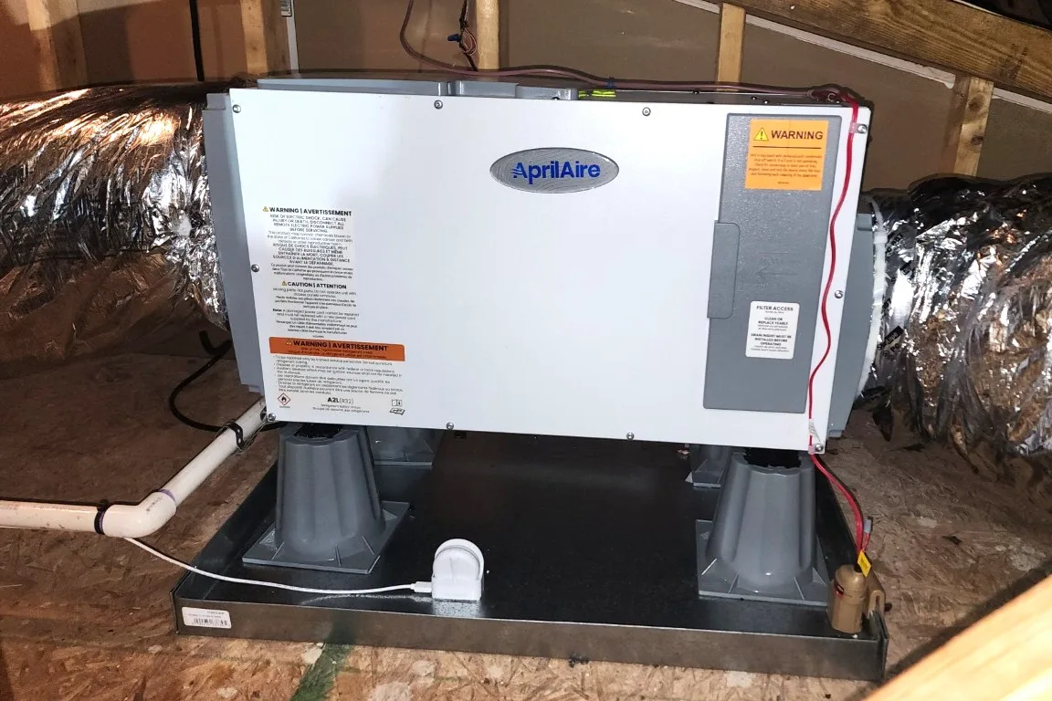 AprilAire whole-house dehumidifier mounted on risers in a drain pan in a Raleigh NC attic